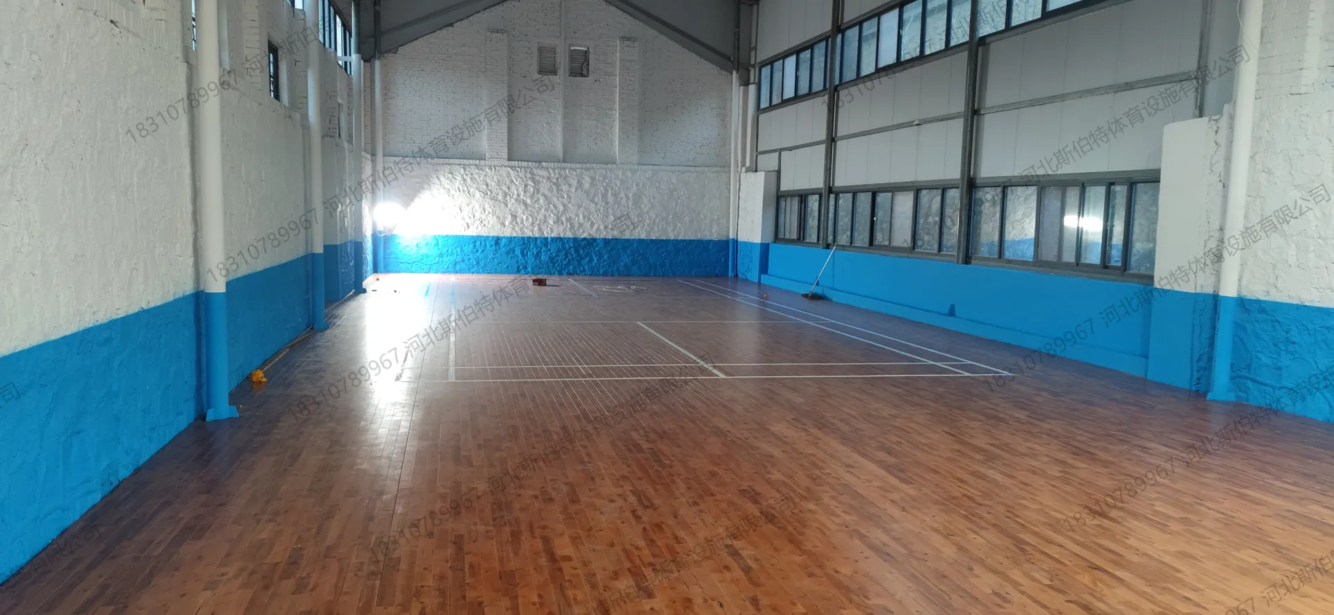 完工实景：深棕色木地板与白色标线对比，蓝色墙裙防撞，高窗自然采光