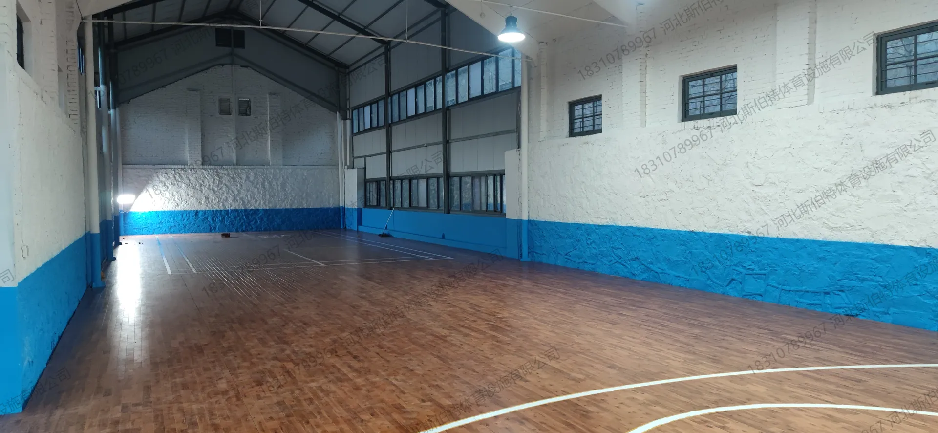 完工实景：地板铺装完成，篮球场中圈标线清晰，钢桁架屋顶外露，高窗采光