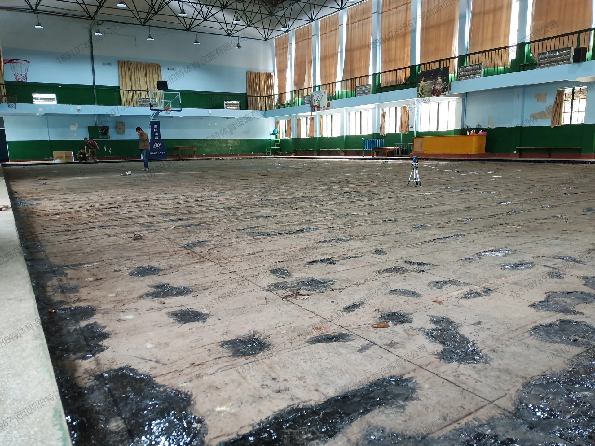 施工前实景：水泥地面破旧不平，三脚架测绘定位，二层看台与羽毛球宣传画原貌