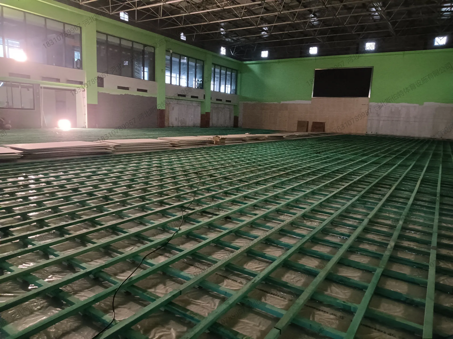双层龙骨完成：绿色龙骨网格铺满场地，面板材料堆放待装
