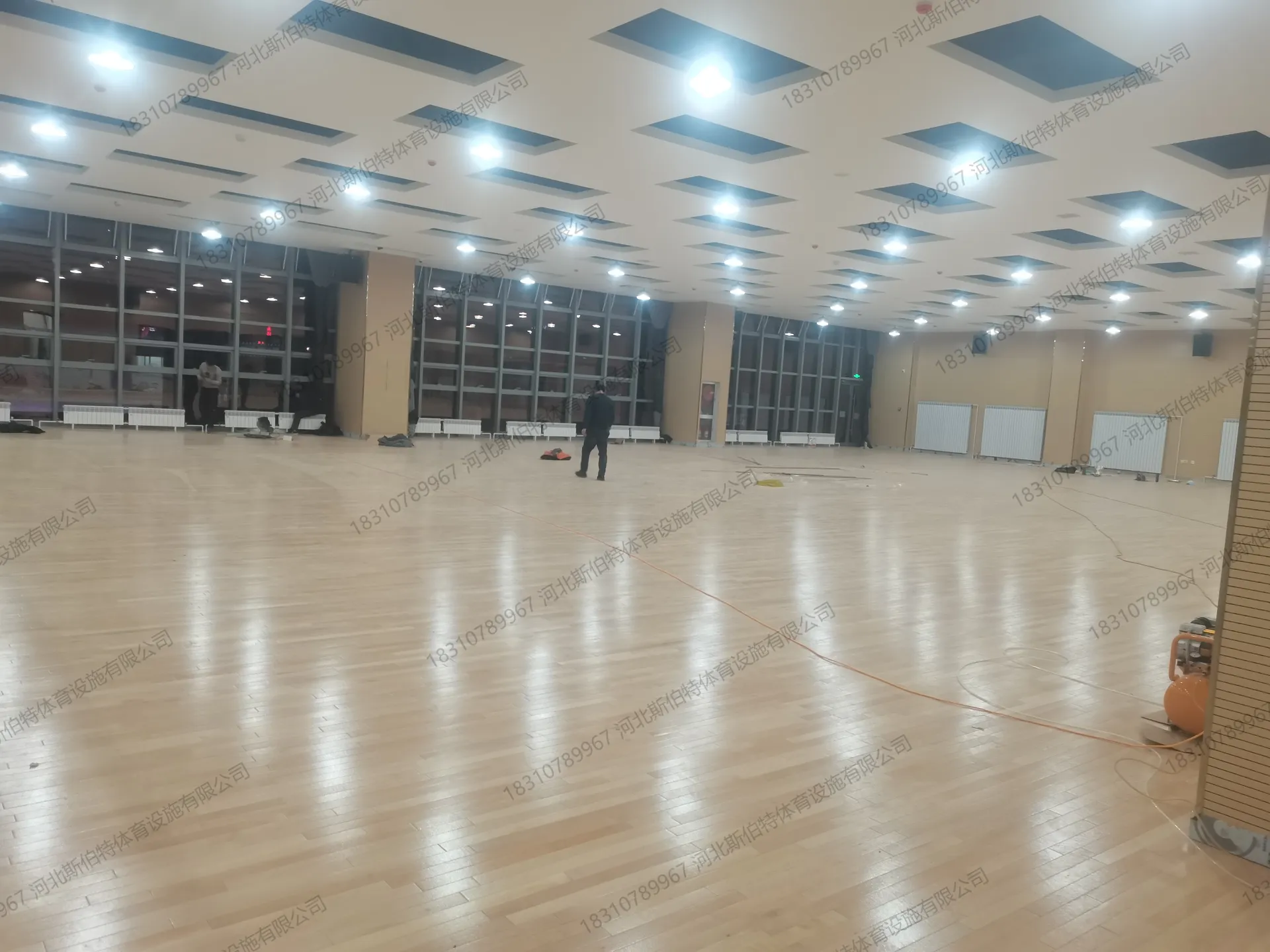 面板铺装完成：浅色原木色地板铺满，场馆空间开阔，施工收尾中