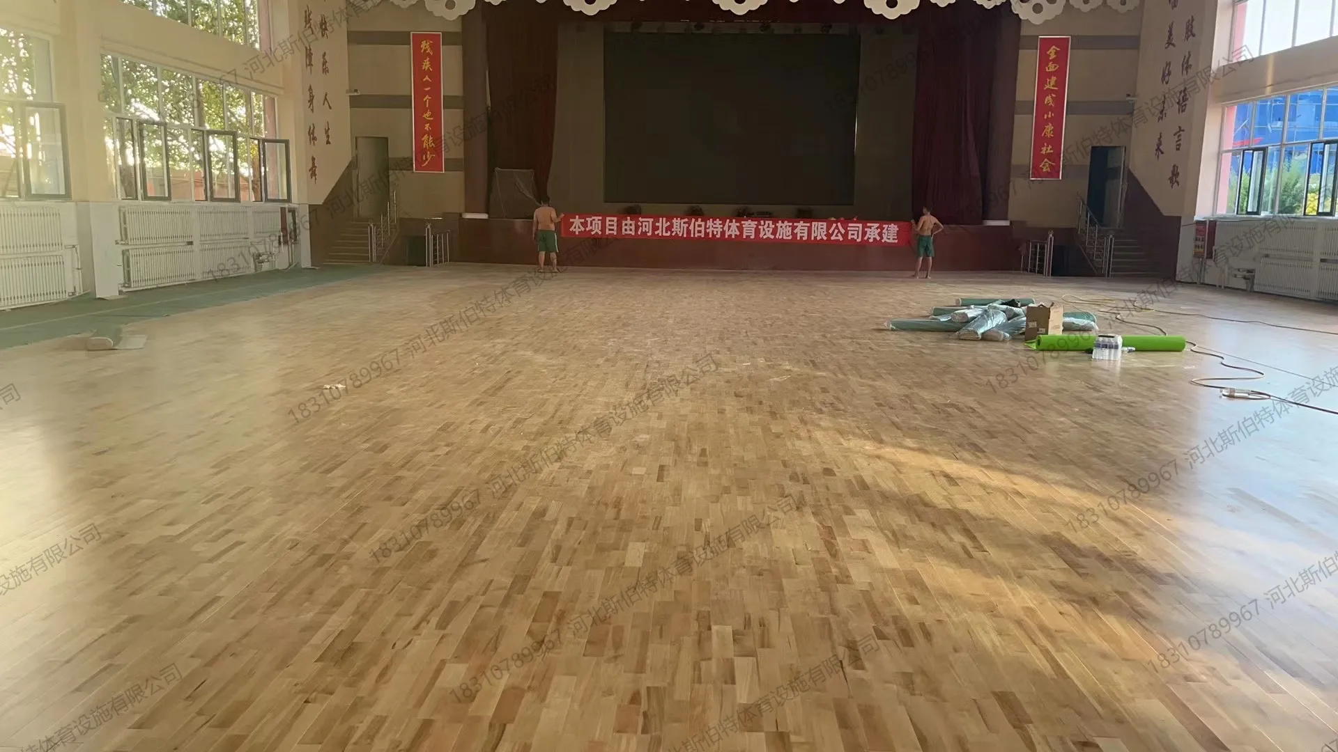 面板铺装完成,礼堂舞台与幕布,红色竖幅标语"一个也不能少""全面建成小康社会"