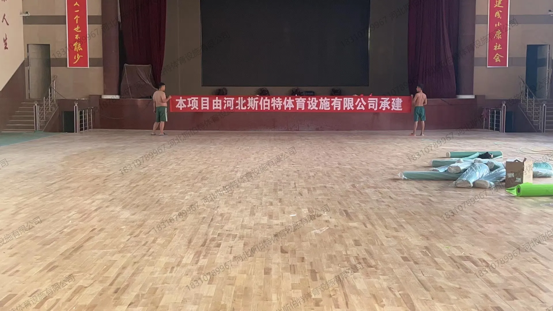 从舞台侧看面板铺装完成,施工方横幅"本项目由河北斯伯特体育设施有限公司承建"