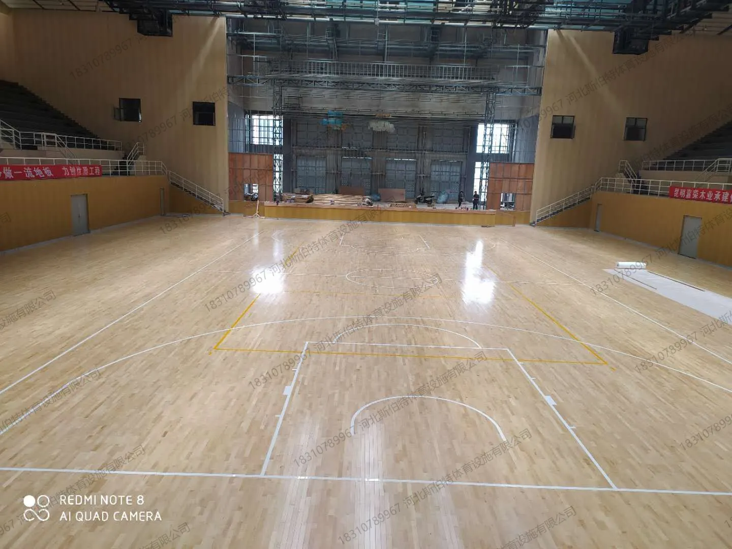 完工实景:枫桦木A级地板铺装完成,篮球场白色与黄色标线清晰,远端舞台桁架可见