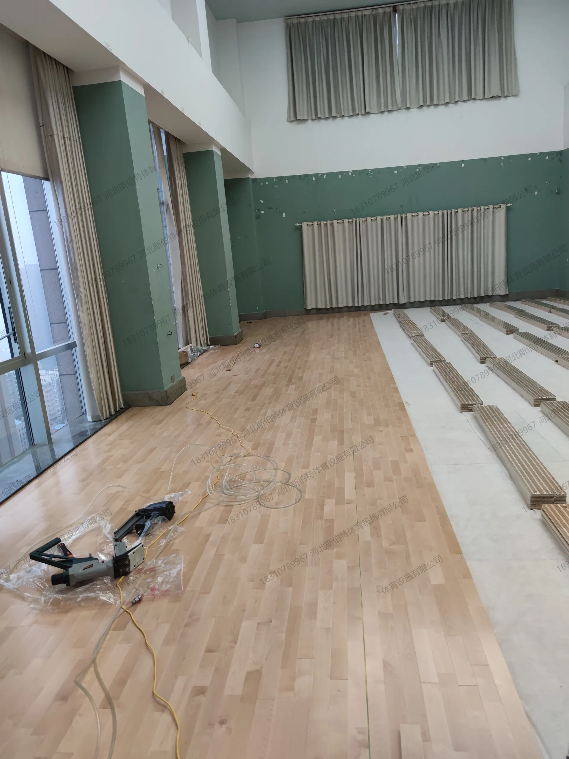 施工过程：面板铺装进行中，气动钉枪固定面板，落地窗借光，深绿色墙面收边