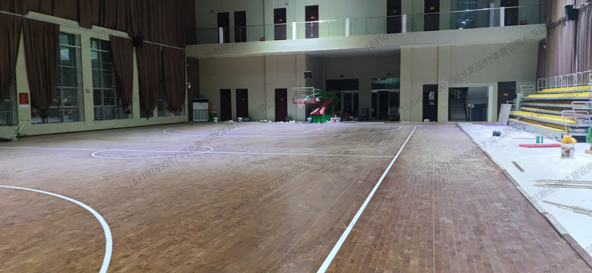 完工实景:篮球场标线完整,阶梯式观众看台黄色座椅,落地窗配深棕色窗帘,县级体育中心场馆氛围
